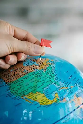 Hand placing a red flag pin on a blue globe — geotargeting