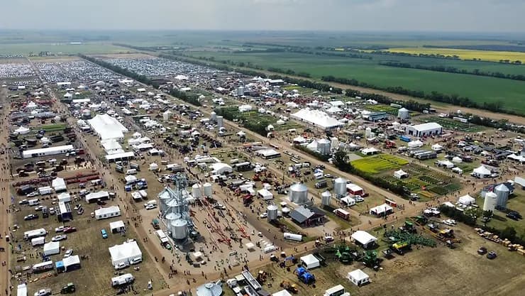 Aerial view of a large outdoor agricultural fair with white tents, farm machinery, and people