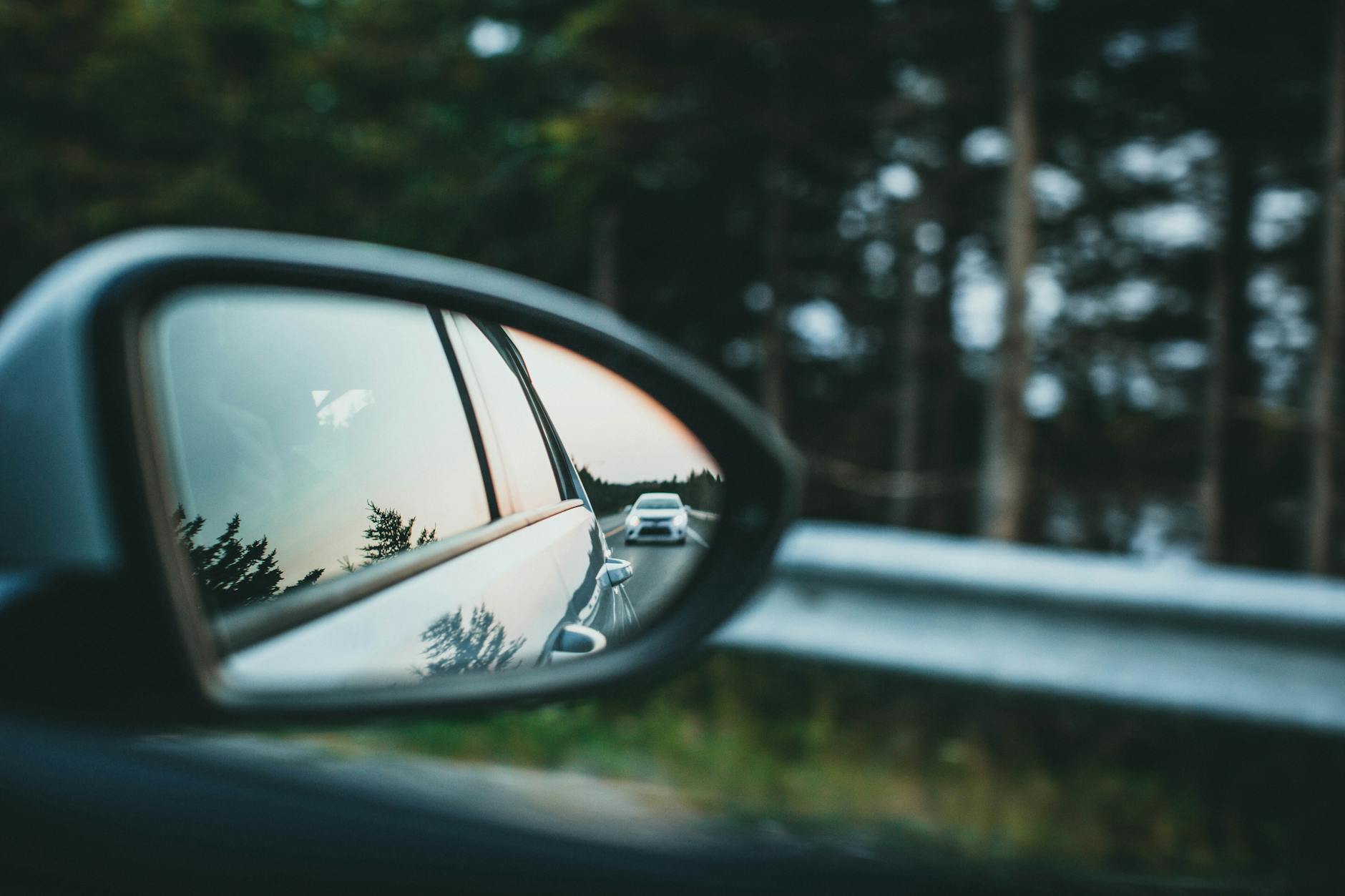 Car reflected in a side mirror on a forest road