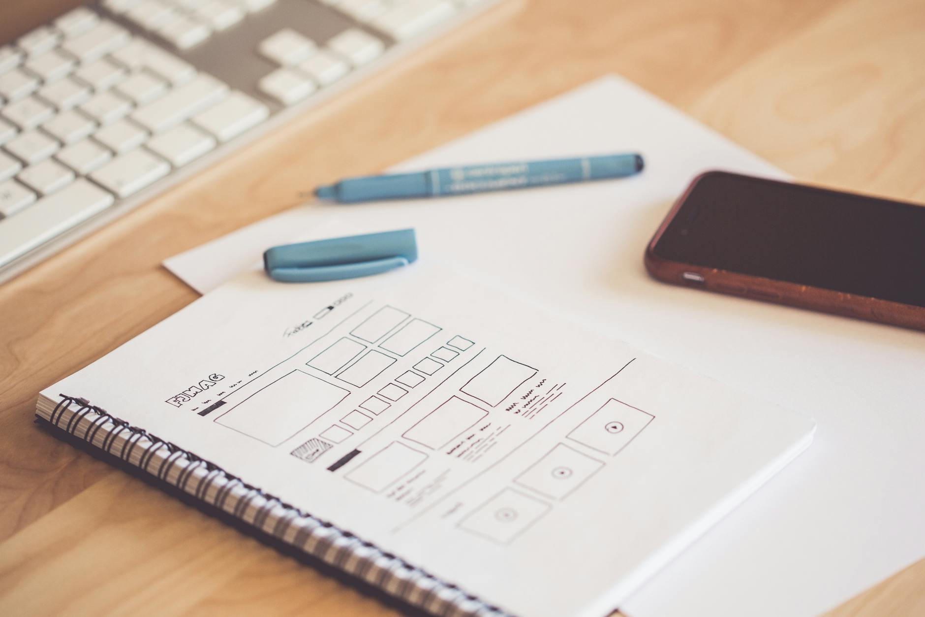 Website wireframe sketches beside a phone and keyboard