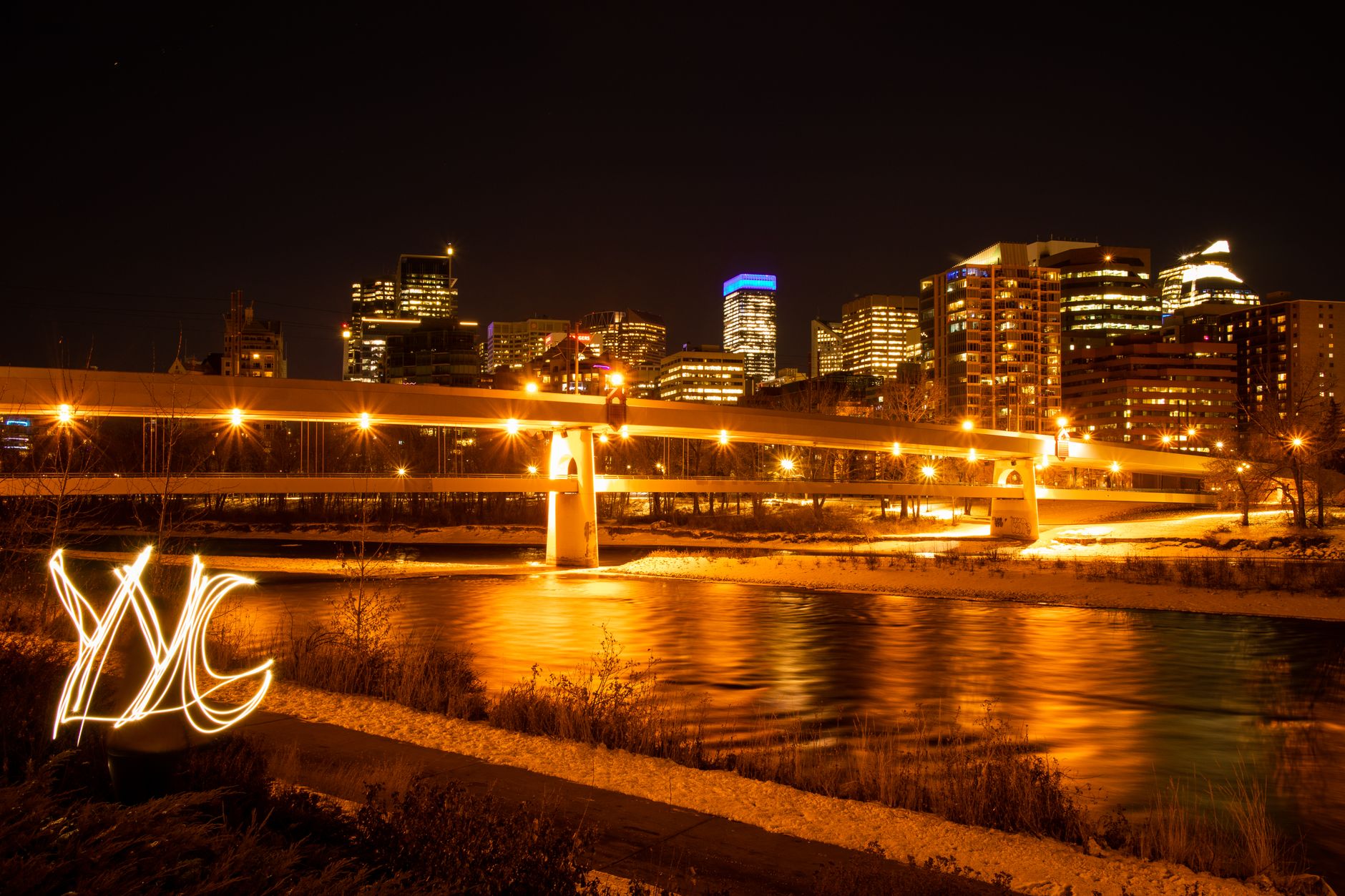 Stunning nighttime view of Calgary's skyline with reflection and bridge lights.