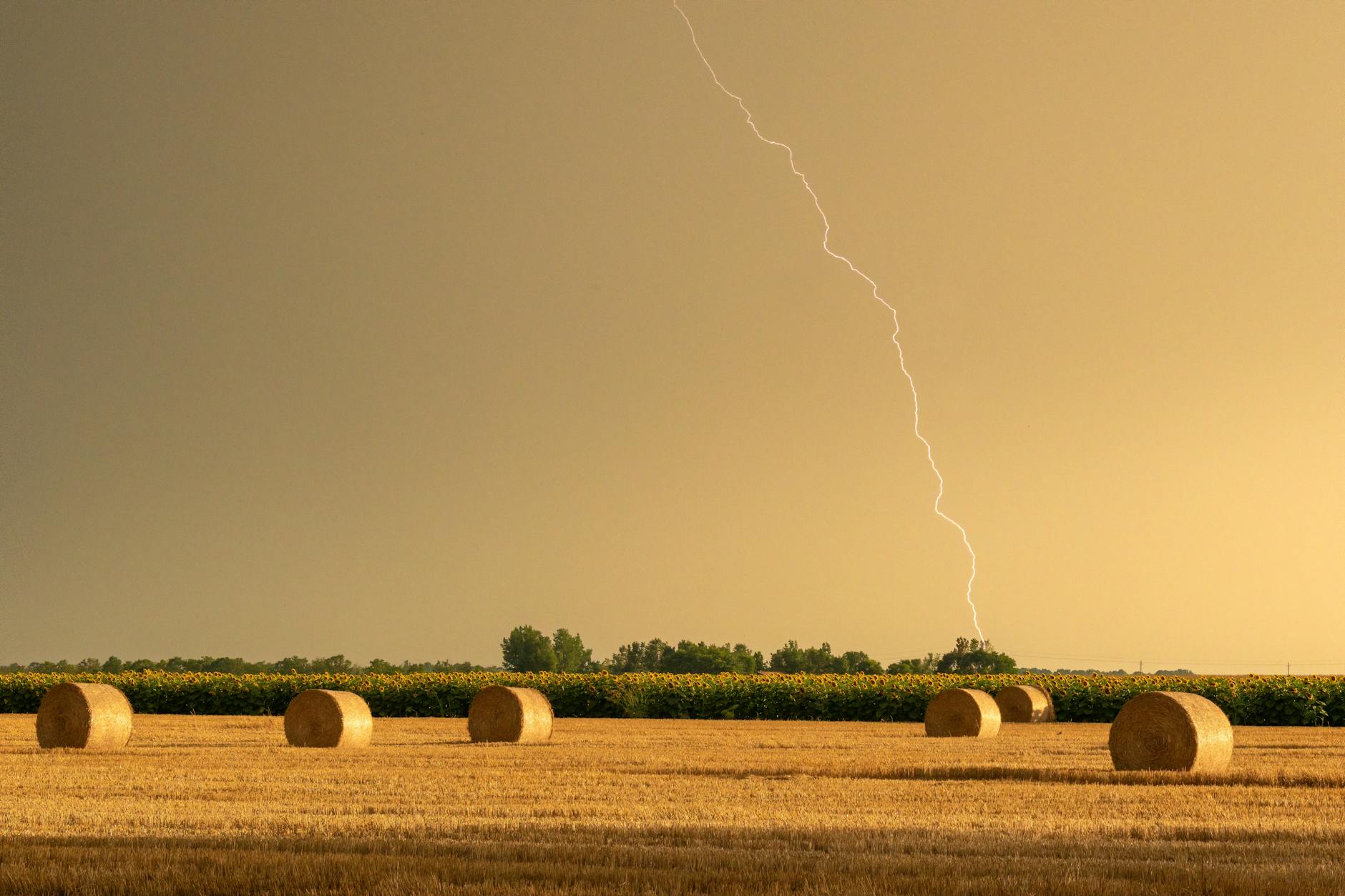 Striking rural landscape featuring hay bales under a dramatic sky with lightning.