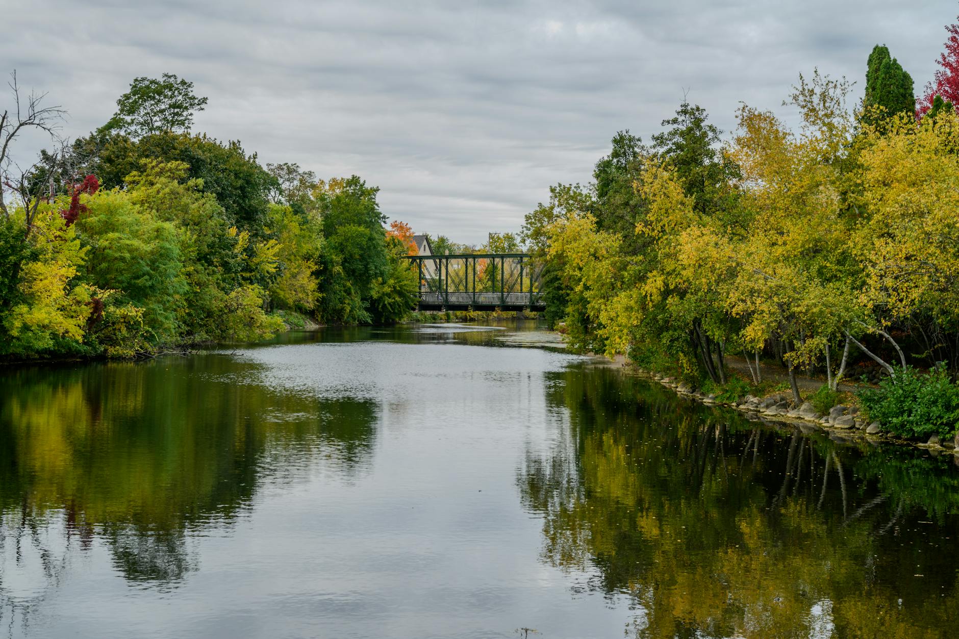 Tranquil autumn river scene with a bridge and colorful foliage.